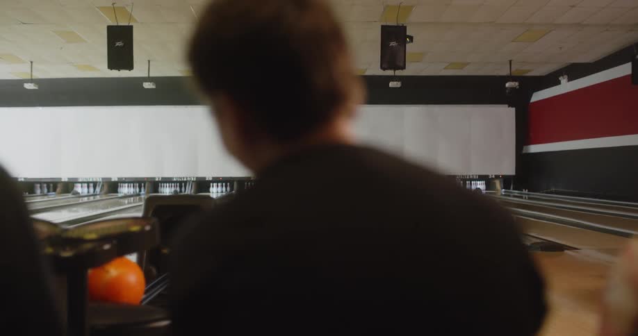 A woman in a yellow dress playing bowling and she looks back where there are some people looking at her