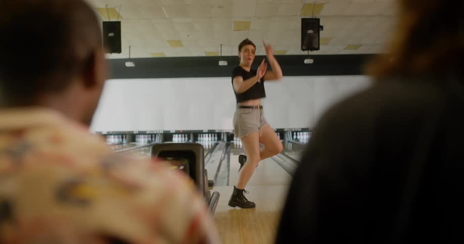 Woman throwing a bowling ball and jumping for joy with her friends in the background watching