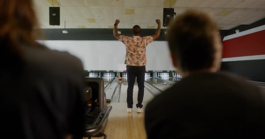 Man throwing a ball in a bowling game and his friends sitting cheering