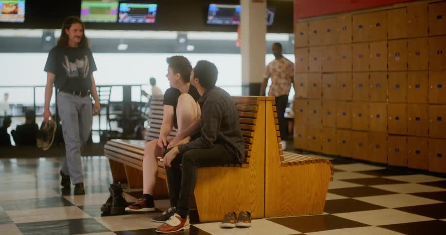 Group of friends sitting on a bench in a bowling zone talking and smiling