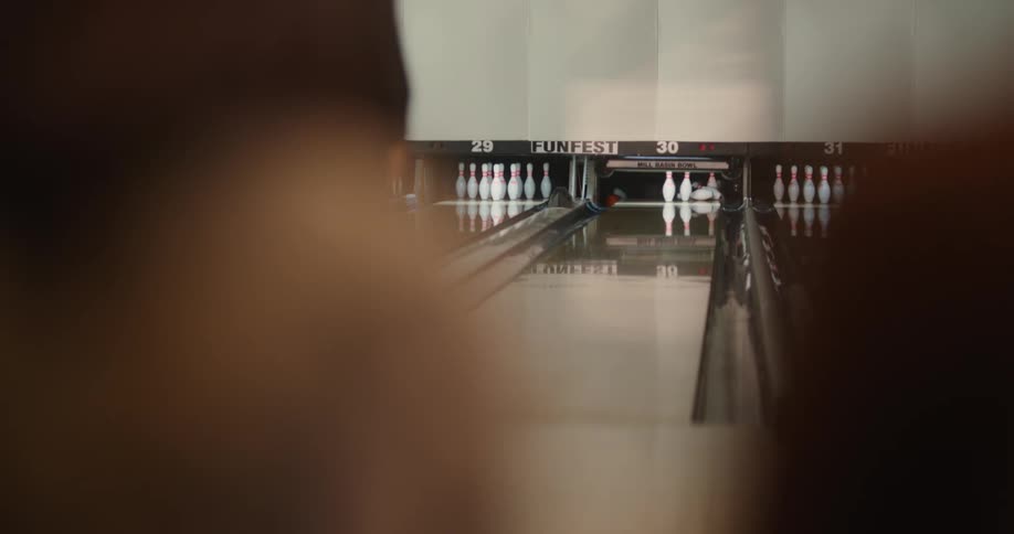 A man in a bowling alley throws a ball down a lane knocking out all but one pin and turns around disappointed