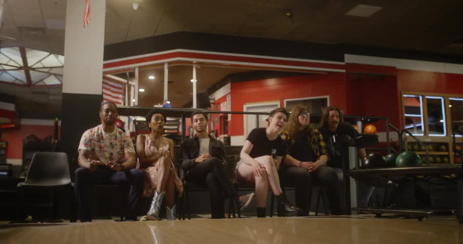 A group of friends in a bowling alley watches as one of them throws a ball and they all celebrate when she comes backl