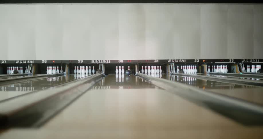 A person wearing a yellow dress throwing a green ball in a bowling alley hitting a white pin