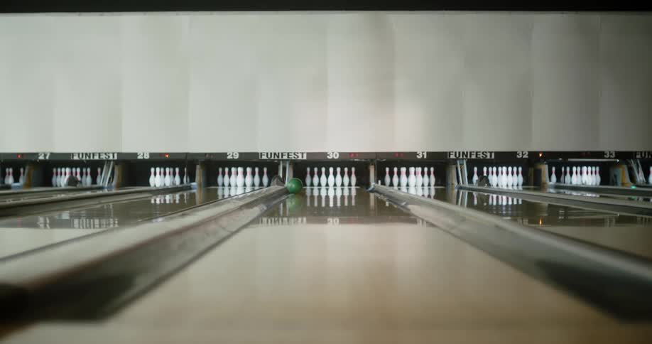 A person throwing a green ball in a bowling alley and it doesnt hit any of the white pins
