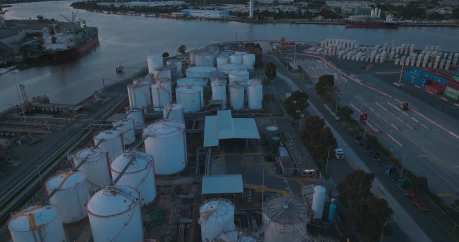 Aerial view of an industrial area at dusk with several large storage tanks and a cargo ship docked nearby