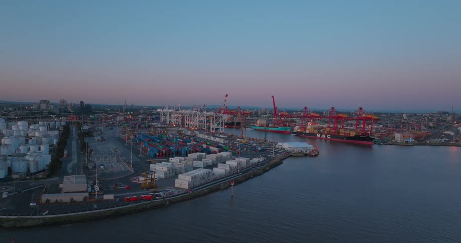 Aerial view of a port during twilight with numerous colorful containers large cranes and cargo ships docked