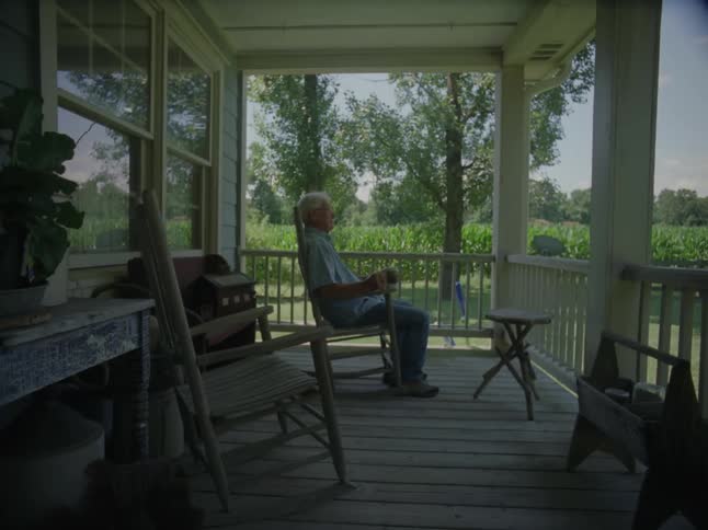A man is sitting on a rocking chair on the porch
