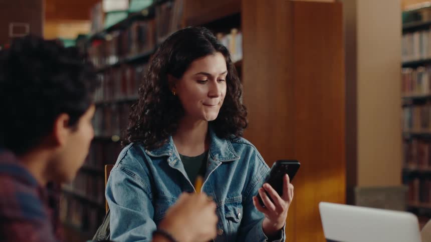 Friends studying sitting at a library table with a woman using a cell phone