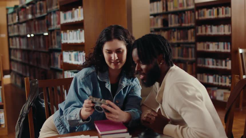 Woman takes a selfie with her friend while sitting at a table in the library