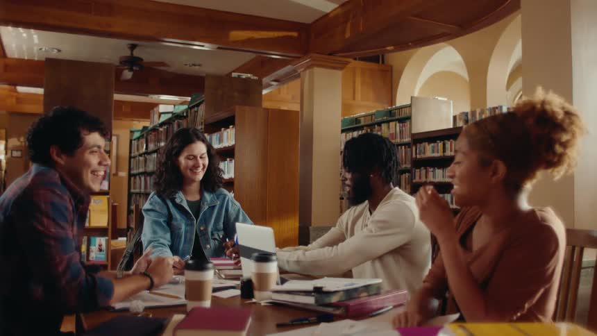 A group of individuals collaborating during a study session at a library smiling and laughing