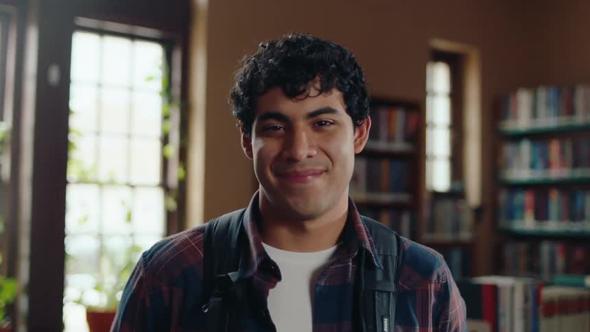 Portrait of latino student in library with backpack softly smiling