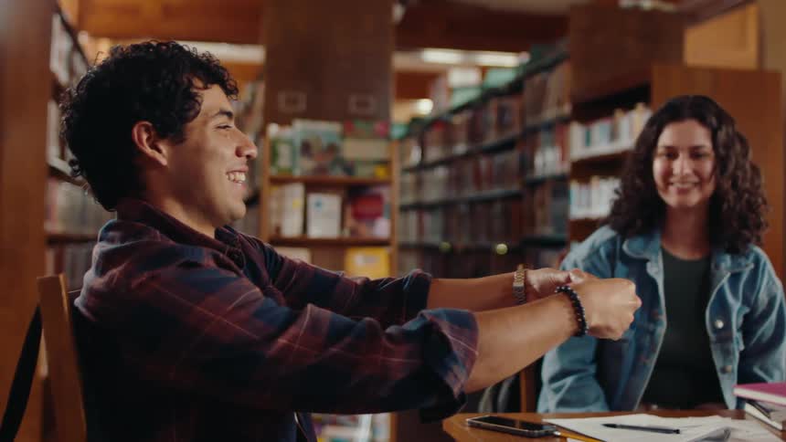 A young man is smiling with a young woman sitting next to him as another man tries to throw a paper ball in his hand