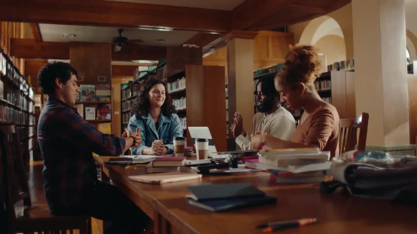 Group of friends sitting at a table in a library talking and playing paper balls