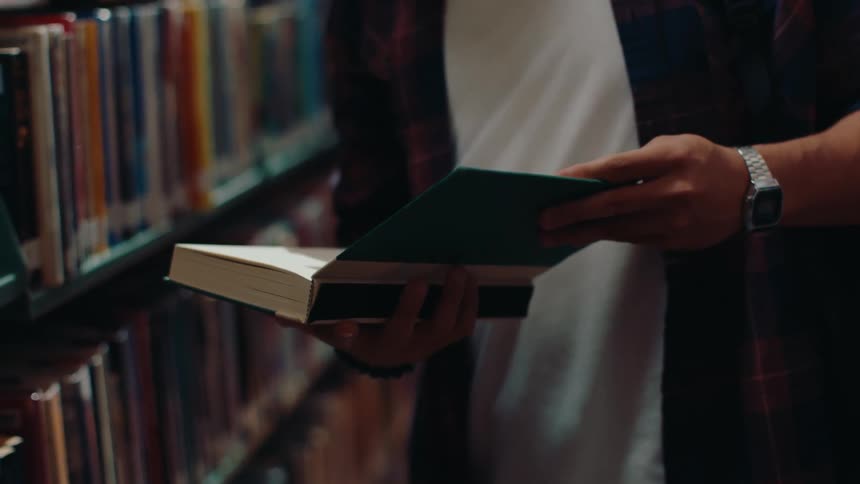 A male student opens a book in a library and smiles