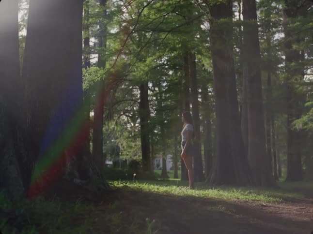 Young woman stands in the woods while traffic passes in the background
