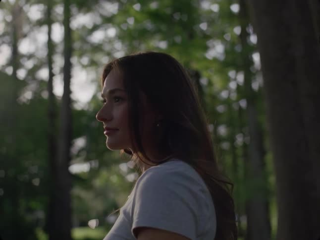 The face of a young woman who is looking forward where there are several trees