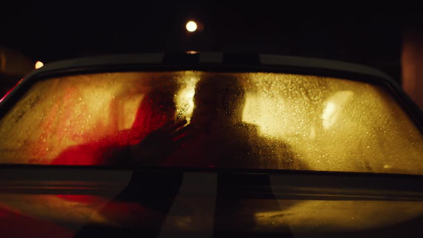 Silhouette of two people inside a car with fogged windows kissing at night