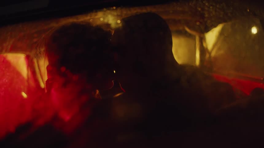 Silhouette of two people inside a car with fogged windows stopped at night kissing