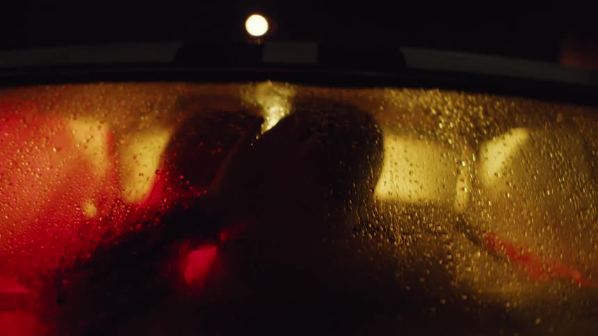 Silhouette of two people kissing warmly inside a car with foggedup windows parked at night