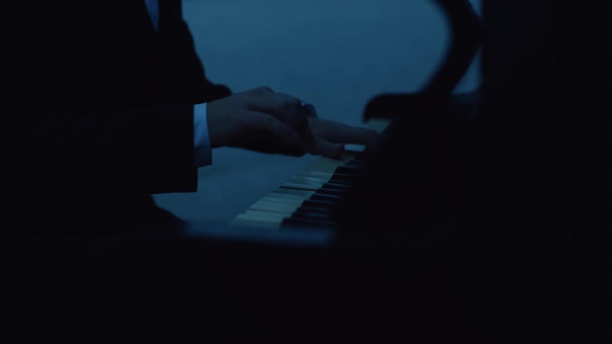 An adult plays a piano next to a body of water at night