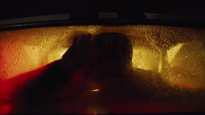 The silhouette of two people kissing inside a car with yellow lights at night