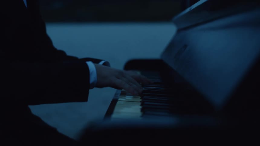 A man in a tuxedo playing a piano at dusk next to a body of water