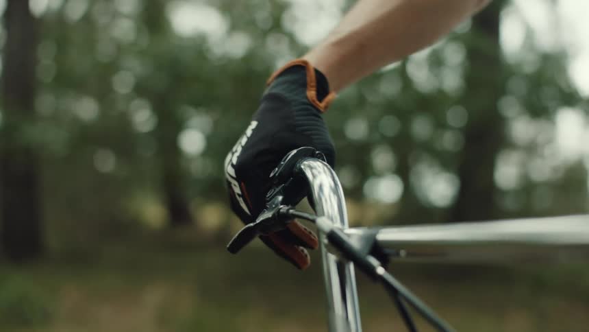A persons hand wearing black gloves holding a silver bicycle handlebar