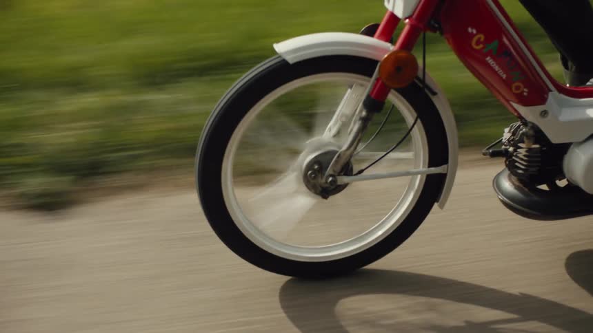 Two people ride a moped on a concrete path