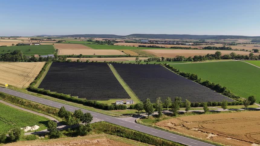 Aerial view of solar panels in an agricultural field next to a highway with vehicle traffic