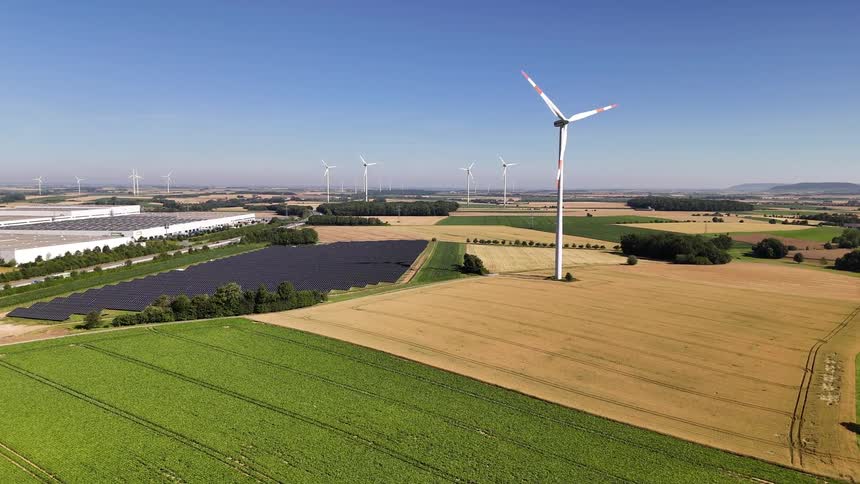 Windmills spin and solar panels generate power near farm fields and a busy highway
