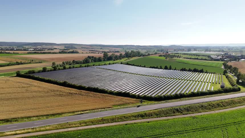 A large lot with a solar panel farm in a rural region next to a road with a car passing by