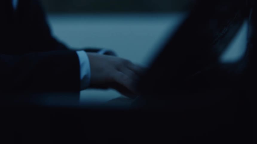 The hands of a person wearing black clothes playing the keys of a black piano