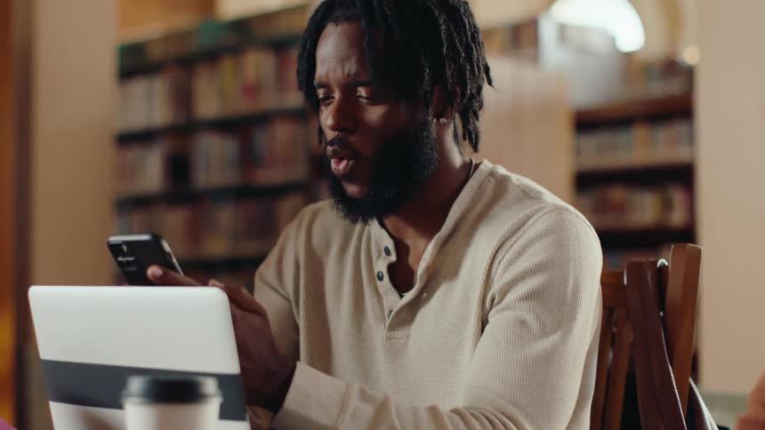 A student picks up his cell phone looks at the screen with happy surprise and responds to the message