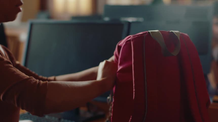 A woman in a library turns to reach for her pink backpack and searches for something