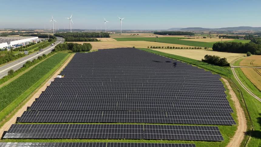 Aerial panorama of solar panels in a field with wind energy turbines in the background
