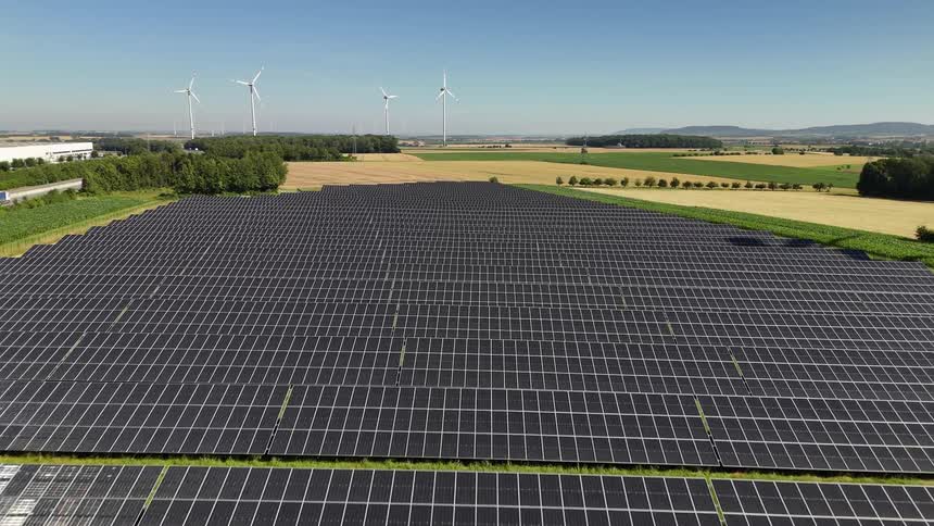 Aerial view of a vast field with solar panels and moving wind energy turbines