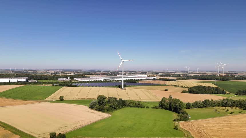 Aerial view of a blue sky and wind energy turbines in natural and agricultural fields
