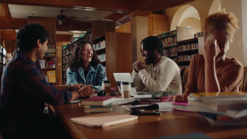 Four friends sitting at a table in a library talking and laughing