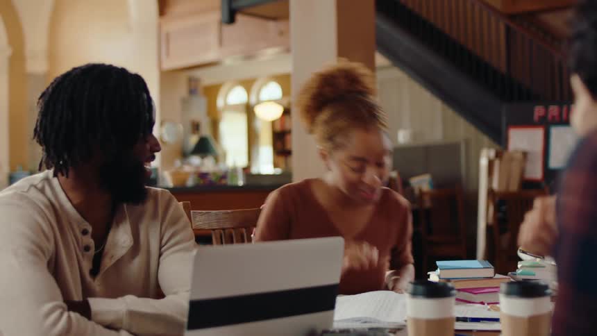 Four students gather around a table in a library and have a conversation