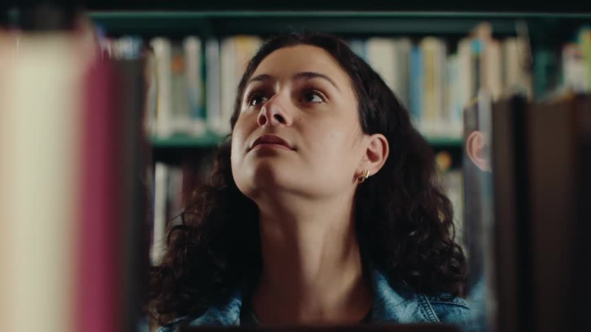 Young woman choosing a book from a library shelf
