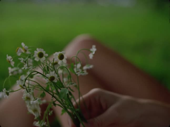Woman sitting outdoors in a field separates a handheld bunch of flowers