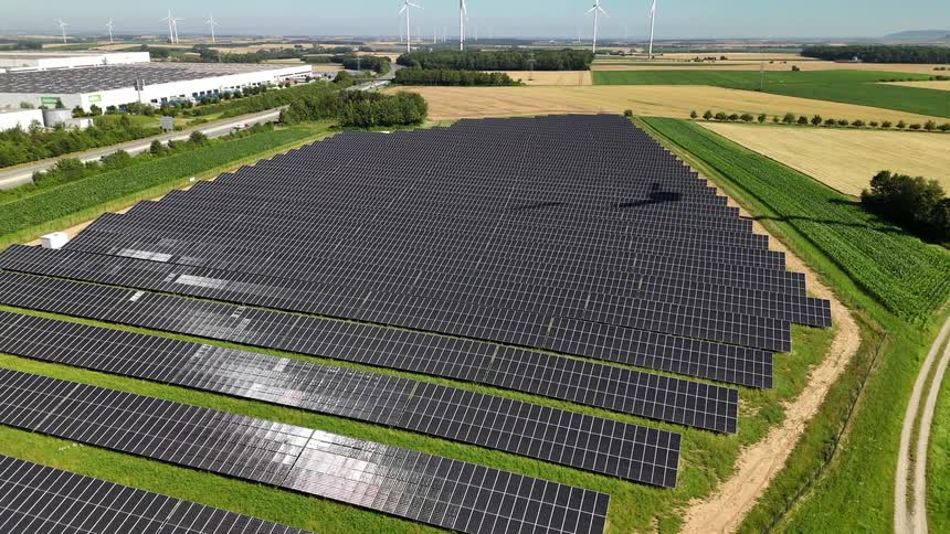 A large field of solar panels sitting next to farm fields and a highway