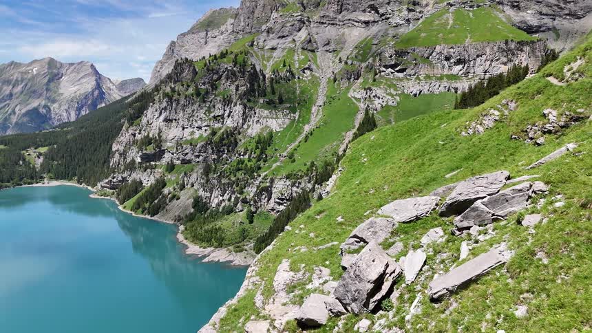 Grass grows on a mountainside next to a lake and a rural community