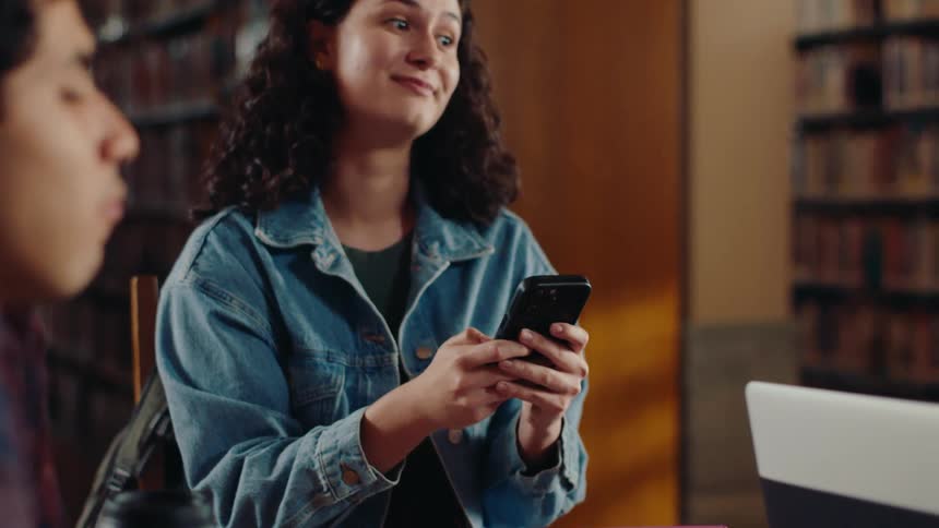 Friends sitting at a table with a woman using her cell phone and then writing on paper