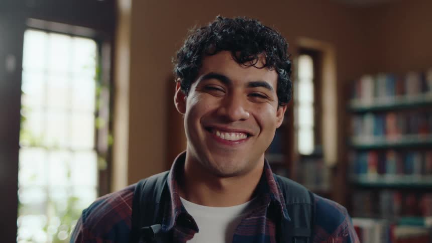 Portrait of latin american male student smiling with backpack in library