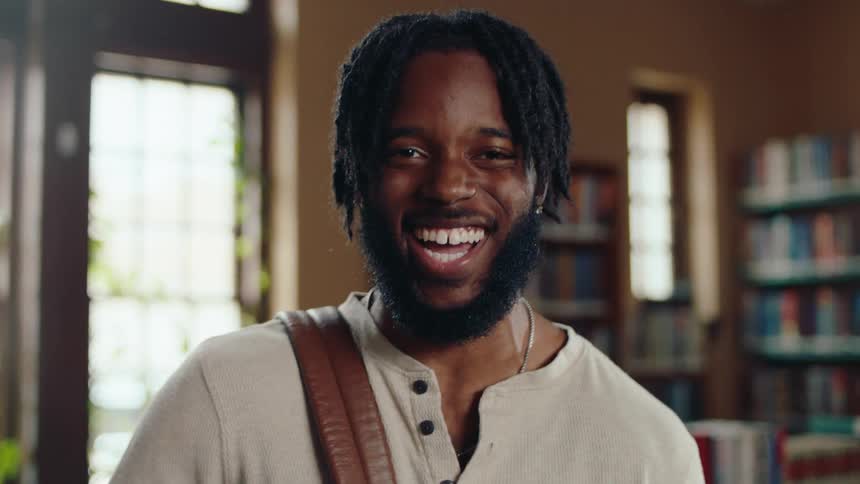 Portrait of young black man with backpack laughing in a library