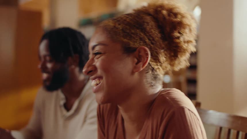 A black man says something that cracks up a black girl sitting next to him in a library