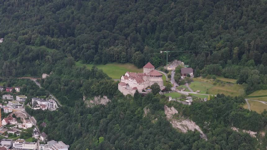 Construction crane stands in the field near a castle at the edge of the forested cliff near town