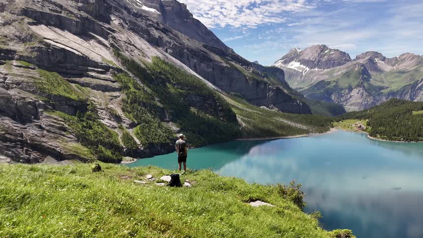 A man stands overlooking a lake by some mountains