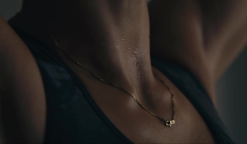 A woman wearing a gold necklace stretches in a gym